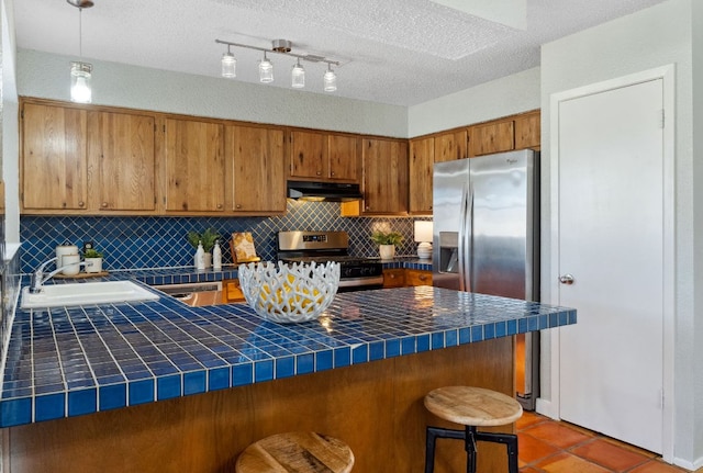 kitchen featuring tile countertops, under cabinet range hood, appliances with stainless steel finishes, and a sink