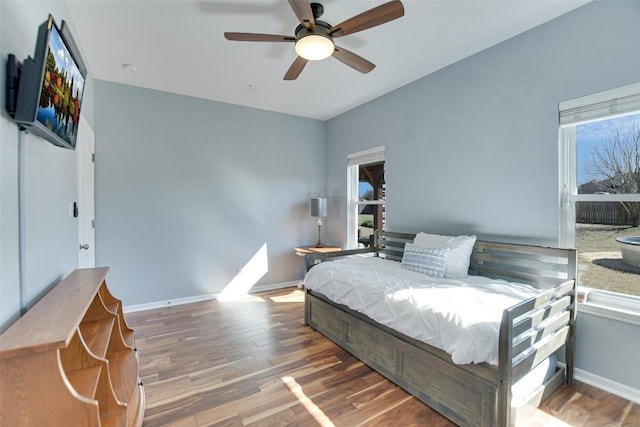 bedroom with multiple windows, wood finished floors, a ceiling fan, and baseboards