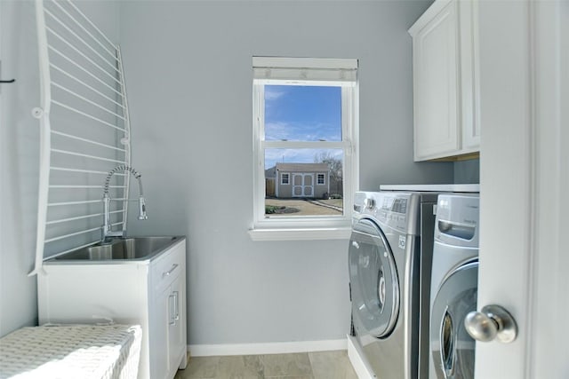 laundry room with washing machine and dryer, cabinet space, a sink, and baseboards