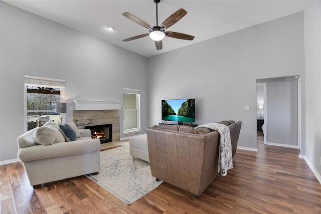 living area with high vaulted ceiling, baseboards, a fireplace with flush hearth, and wood finished floors