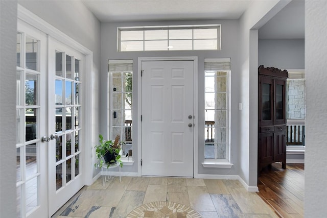 entrance foyer with french doors, a healthy amount of sunlight, baseboards, and wood finished floors