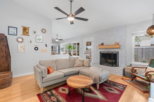 living area with a brick fireplace, plenty of natural light, baseboards, and hardwood / wood-style flooring