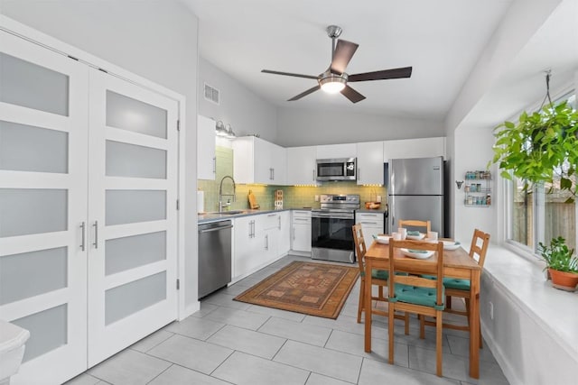 kitchen with stainless steel appliances, a sink, white cabinetry, vaulted ceiling, and backsplash