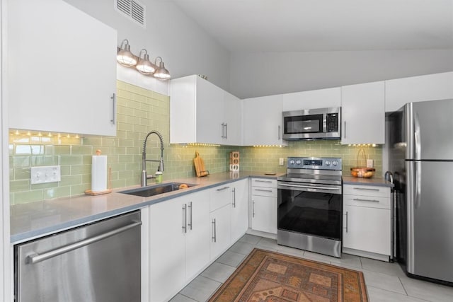 kitchen featuring lofted ceiling, light tile patterned floors, stainless steel appliances, a sink, and tasteful backsplash