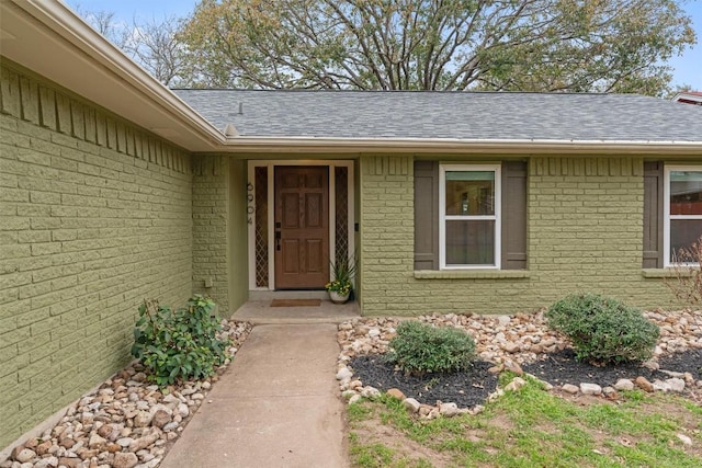 doorway to property featuring a shingled roof and brick siding