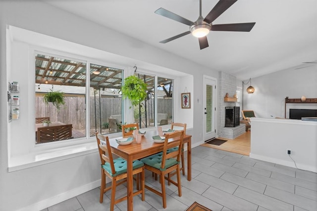 tiled dining area featuring vaulted ceiling, a fireplace, a ceiling fan, and baseboards