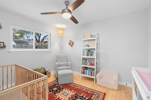 bedroom featuring a nursery area, wood finished floors, a ceiling fan, and baseboards