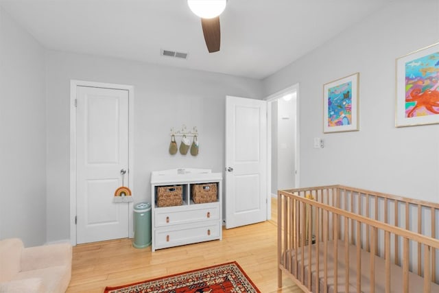 bedroom featuring visible vents, ceiling fan, a crib, and light wood finished floors