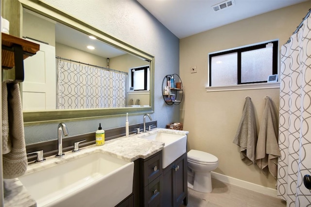 full bath featuring toilet, double vanity, a sink, and visible vents