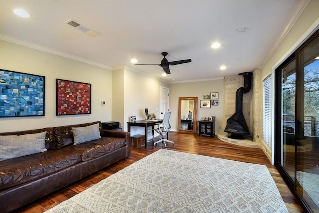 living room with a wood stove, visible vents, wood finished floors, and ornamental molding