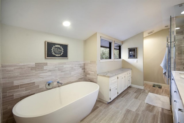 full bathroom featuring lofted ceiling, wood finished floors, a freestanding bath, vanity, and tile walls