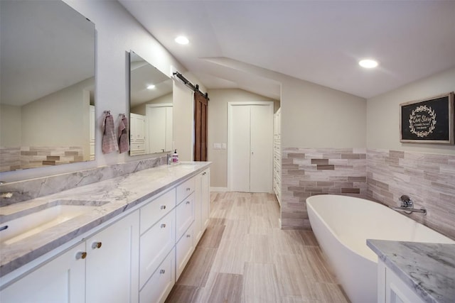 bathroom with recessed lighting, a sink, tile walls, a freestanding bath, and double vanity