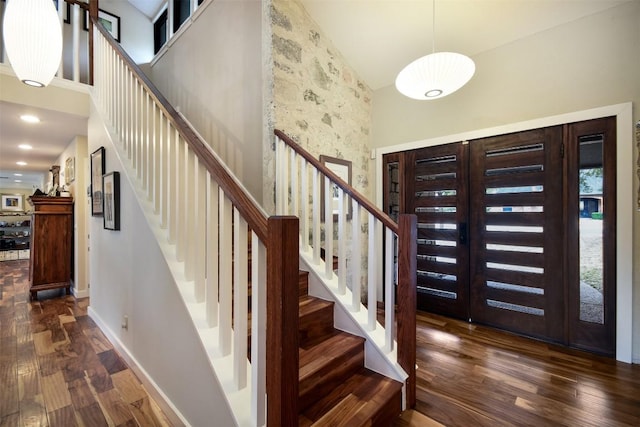 entrance foyer featuring dark wood-style flooring, a towering ceiling, baseboards, and stairs