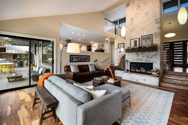 living area featuring a large fireplace, high vaulted ceiling, stairway, and wood finished floors