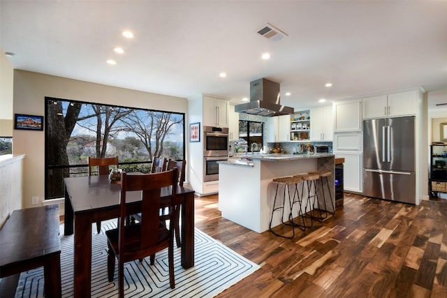 kitchen featuring dark wood finished floors, appliances with stainless steel finishes, white cabinets, a kitchen island, and island range hood