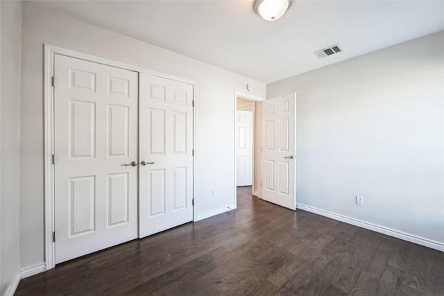 unfurnished bedroom featuring a closet, dark wood finished floors, visible vents, and baseboards