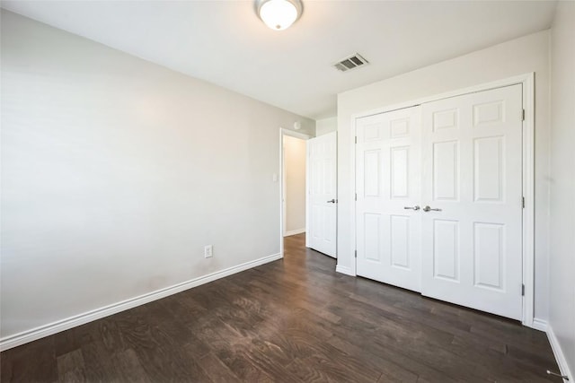 unfurnished bedroom with dark wood-type flooring, a closet, visible vents, and baseboards