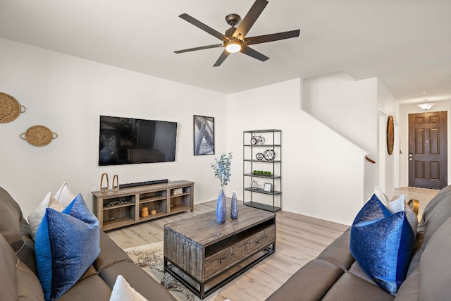 living room featuring baseboards, stairway, light wood-style flooring, and a ceiling fan