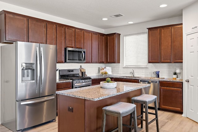 kitchen featuring a breakfast bar area, stainless steel appliances, a sink, visible vents, and light stone countertops