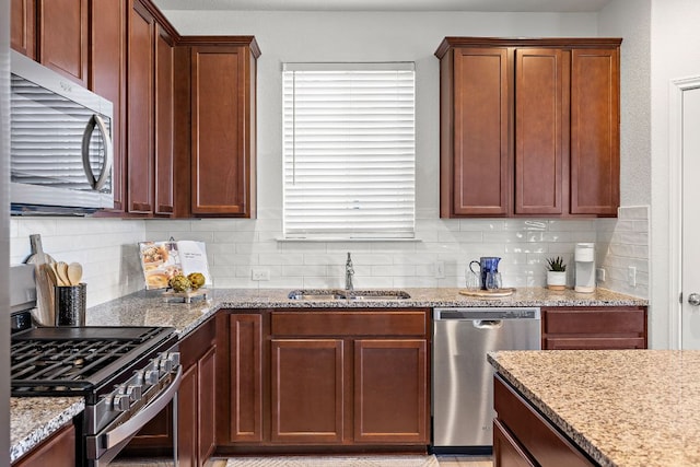 kitchen featuring appliances with stainless steel finishes, decorative backsplash, a sink, and light stone countertops