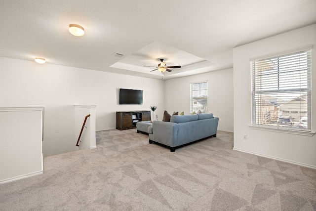 carpeted living area with ceiling fan, a raised ceiling, and visible vents