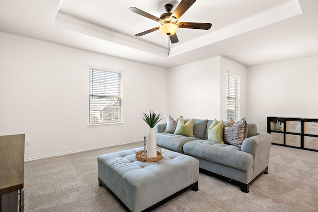 living area featuring light carpet, ceiling fan, a tray ceiling, and ornamental molding