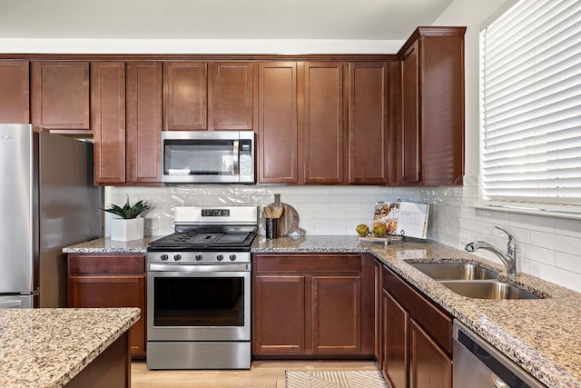 kitchen featuring appliances with stainless steel finishes, a sink, backsplash, and light stone countertops