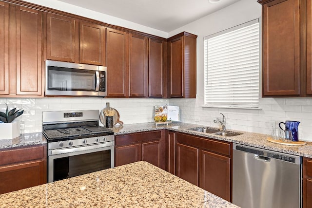 kitchen with light stone counters, a sink, appliances with stainless steel finishes, a wealth of natural light, and tasteful backsplash