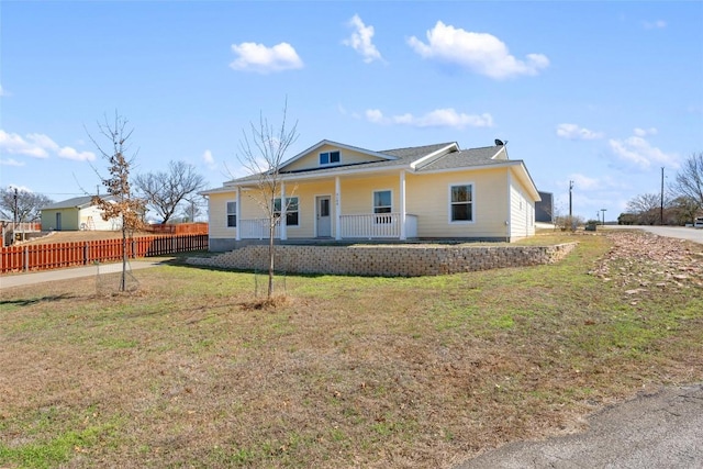 view of front of house featuring covered porch, fence, and a front lawn