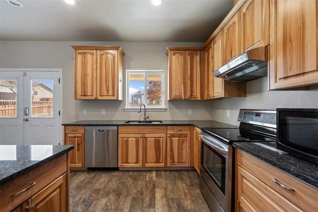 kitchen with dark wood finished floors, dark stone counters, stainless steel appliances, under cabinet range hood, and a sink