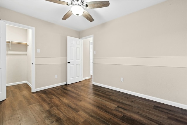 unfurnished bedroom featuring dark wood finished floors, a closet, a spacious closet, a ceiling fan, and baseboards