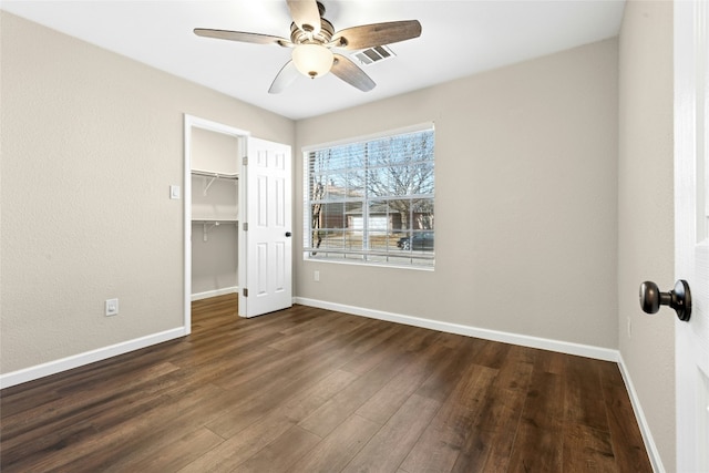 unfurnished bedroom featuring dark wood-style floors, visible vents, a spacious closet, and baseboards