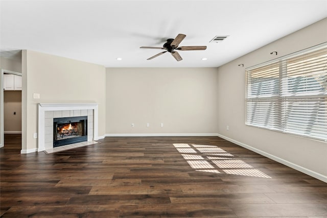 unfurnished living room with wood finished floors, a ceiling fan, visible vents, baseboards, and a tiled fireplace