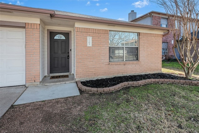 view of exterior entry with a garage, brick siding, and a chimney