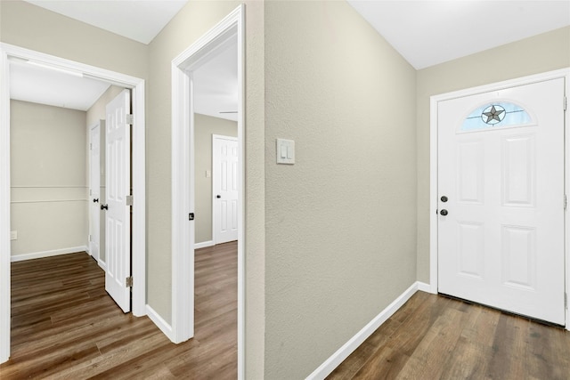 foyer with dark wood-style flooring, a textured wall, and baseboards