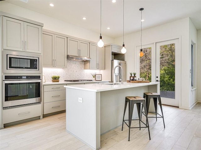 kitchen featuring under cabinet range hood, tasteful backsplash, stainless steel appliances, and gray cabinetry