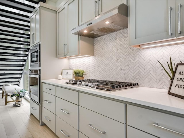 kitchen with stainless steel appliances, gray cabinets, light countertops, and under cabinet range hood