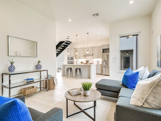 living room with stairs, light wood-type flooring, visible vents, and recessed lighting