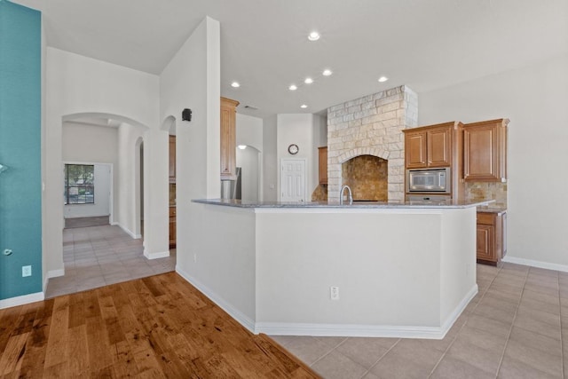 kitchen with arched walkways, light tile patterned flooring, backsplash, light stone countertops, and stainless steel microwave