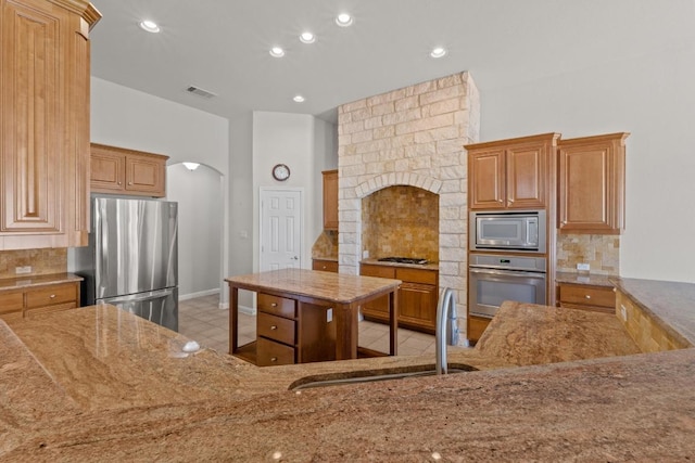 kitchen featuring light stone countertops, arched walkways, stainless steel appliances, and a sink