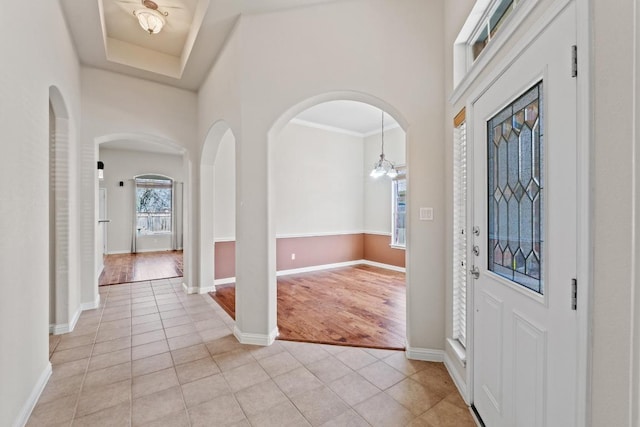 entrance foyer featuring a towering ceiling, light tile patterned floors, baseboards, and arched walkways