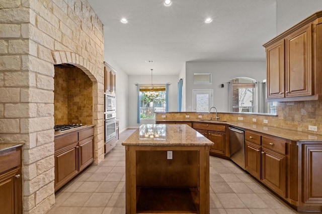 kitchen featuring stainless steel appliances, a peninsula, a sink, decorative backsplash, and brown cabinetry