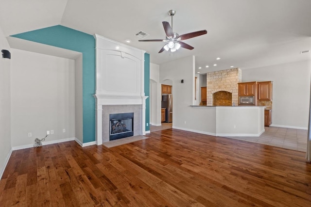 unfurnished living room featuring a large fireplace, a ceiling fan, visible vents, and wood finished floors