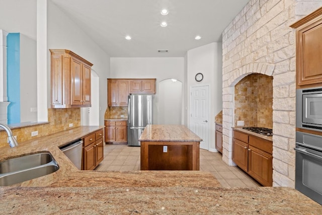 kitchen with stainless steel appliances, decorative backsplash, light tile patterned flooring, a sink, and light stone countertops