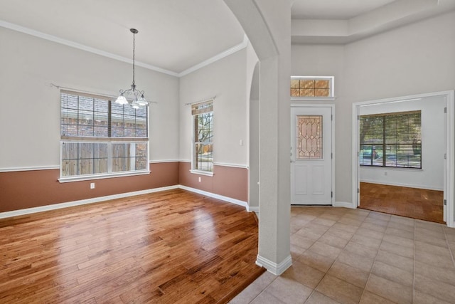 entrance foyer with arched walkways, crown molding, an inviting chandelier, wood finished floors, and baseboards