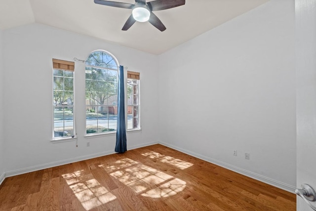 empty room with ceiling fan, vaulted ceiling, wood finished floors, and baseboards