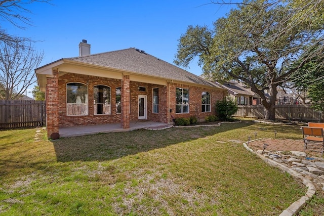 rear view of house featuring a patio, brick siding, fence, a lawn, and a chimney