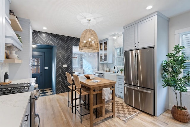 kitchen featuring recessed lighting, light wood-style floors, hanging light fixtures, appliances with stainless steel finishes, and glass insert cabinets