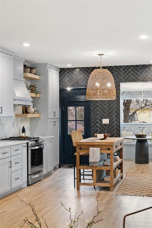 kitchen featuring open shelves, stainless steel gas range oven, decorative backsplash, light wood-type flooring, and pendant lighting