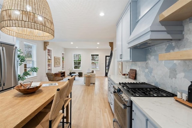 kitchen featuring appliances with stainless steel finishes, custom exhaust hood, light stone counters, and a healthy amount of sunlight